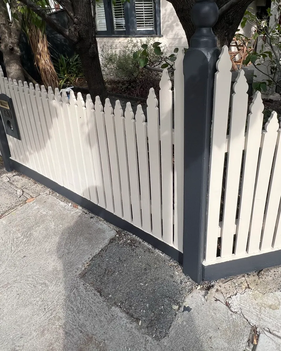 A freshly painted two-tone picket fence and gate in front of a period cottage